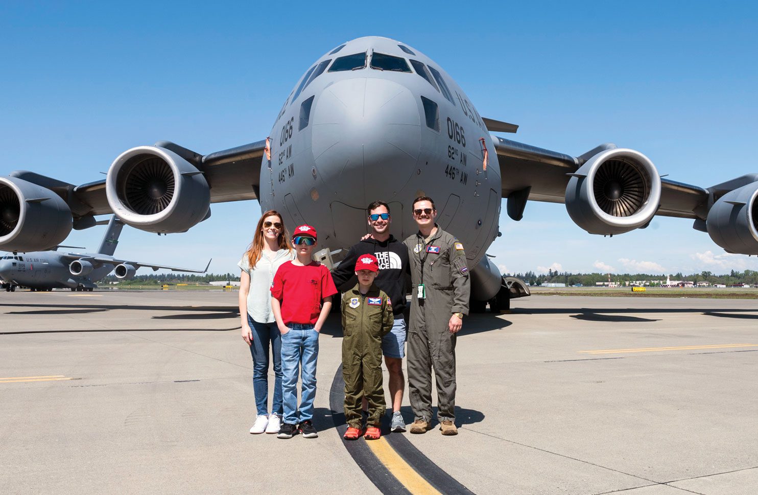 A family with two boys stand with an Airman in front of an aircraft.