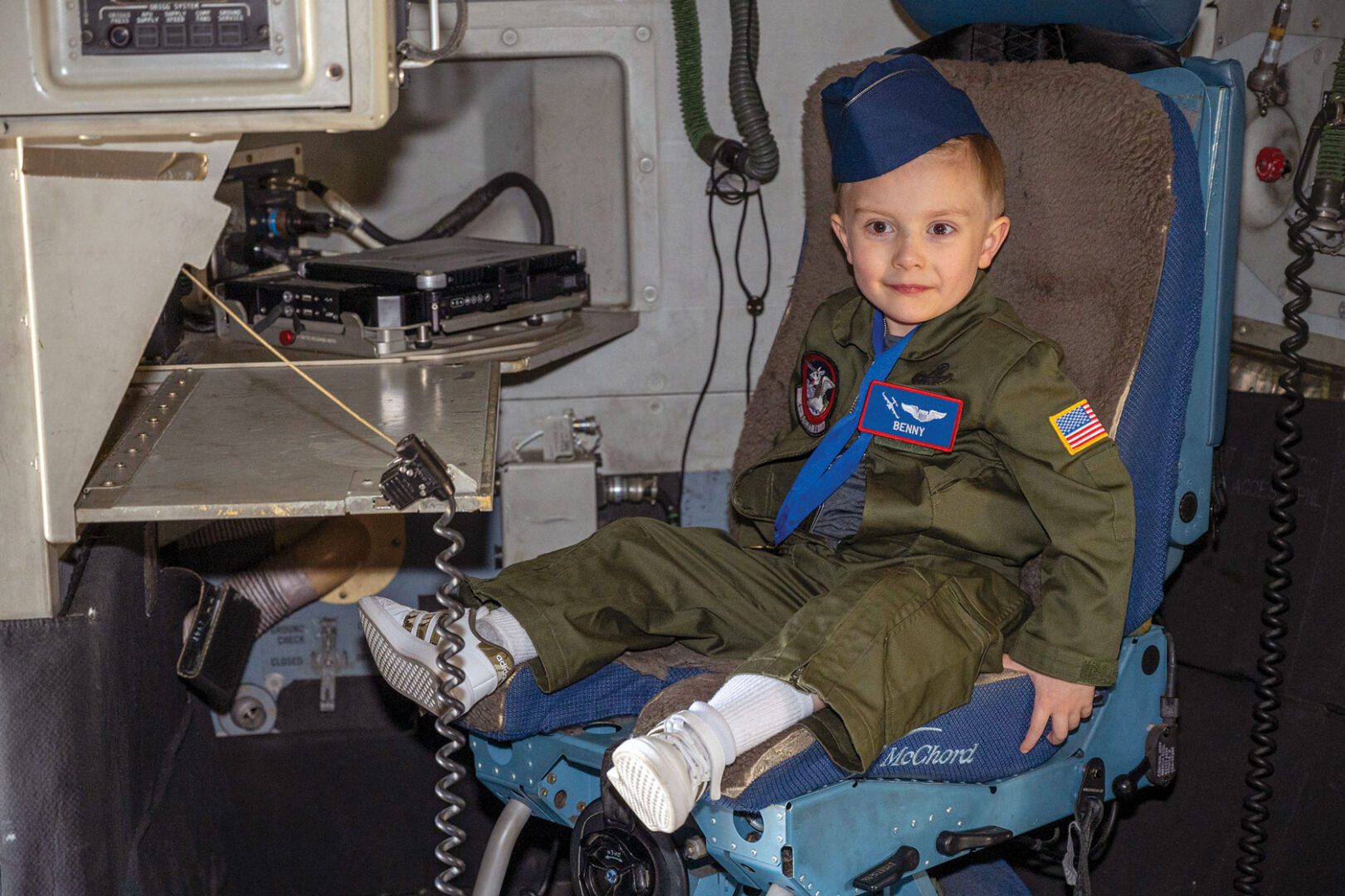 A young child wearing a pilot uniform sits in an aircraft.