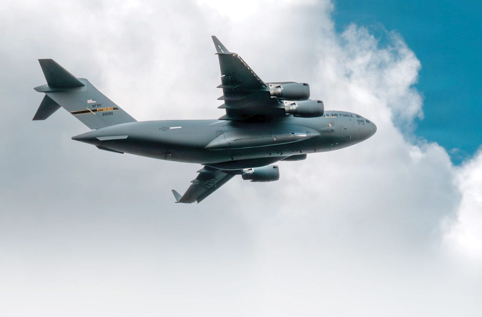 A C-17 Globemaster III aircraft flying in the sky with clouds in the background.